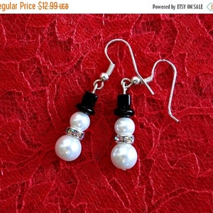 May include: A pair of silver snowman earrings with white pearl beads, black bead hats, and clear rhinestone accents.