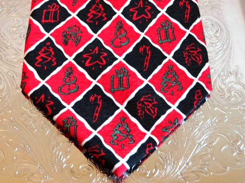 May include: A red and black patterned tie with a diamond pattern featuring Christmas-themed symbols like presents, candy canes, stars, and Christmas trees.