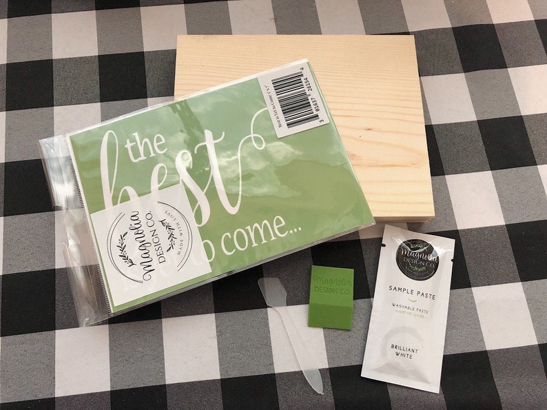 May include: A green stencil with the text "the best is to come..." and a white circle with the text "Magnolia Design Co."  A wooden sign, a green sample of paint, and a white packet of sample paste are also included.