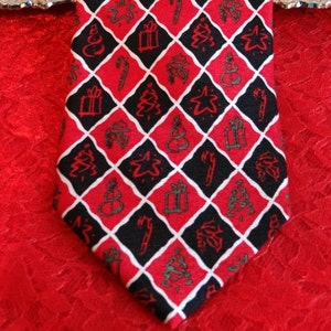 May include: A red, black, and white patterned tie with a Christmas theme. The pattern includes Christmas trees, stars, snowmen, presents, and candy canes.