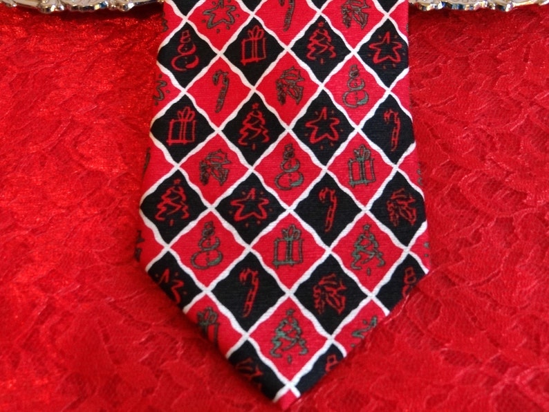 May include: A red, black, and white patterned tie with a Christmas theme. The pattern includes Christmas trees, stars, snowmen, presents, and candy canes.