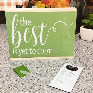 May include: A green wooden sign with white lettering that reads "the best is yet to come".