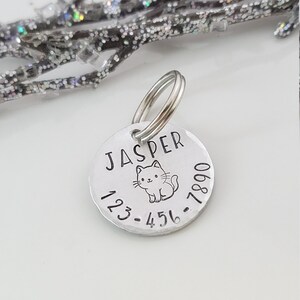 May include: Silver pet ID tag with a cat illustration and the name "Jasper" engraved on it. The tag also includes the phone number 123-456-7890.