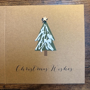 May include: A Christmas card with a green tree design, adorned with white accents and a wooden star. The card is a natural brown color, with the words "Christmas Wishes" written in elegant script.