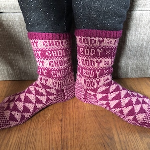 Puede incluir: Un par de calcetines de punto rosa y blanco con un patrón geométrico. Los calcetines tienen las palabras "BODY" y "CHOICE" escritas en ellos.