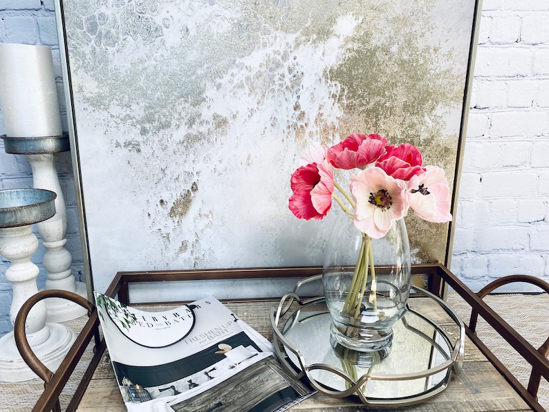 May include: A glass vase filled with pink and white silk flowers sits on a silver tray with a magazine on a wooden surface.