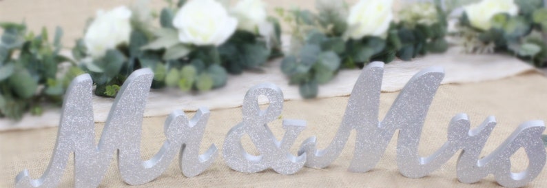 Peut inclure: D&eacute;cor de mariage en bois avec inscription "Mr. & Mrs." en paillettes argent&eacute;es.