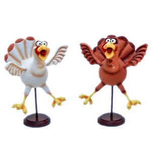 May include: Two whimsical turkey figurines, one white and one brown, with exaggerated features and outstretched wings. They are both standing on black metal stands with brown wooden bases.