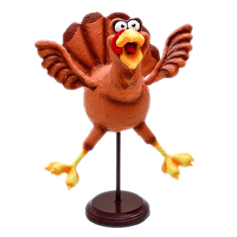 May include: A brown and yellow turkey figurine with a red wattle and large, round eyes. The turkey is standing on a brown wooden base with a black metal rod.