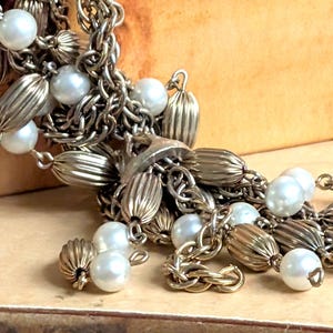 May include: A multi-strand necklace with silver chain and white pearl accents. The necklace features a tassel of silver beads and pearls.