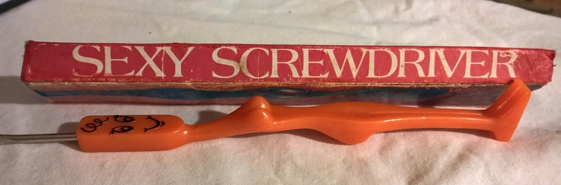 May include: An orange screwdriver with a cartoon face on the handle and the text "SEXY SCREWDRIVER" on the red and white box. The screwdriver has a unique, ergonomic design.
