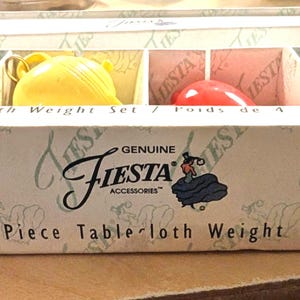 May include: A 4-piece Genuine Fiesta Accessories tablecloth weight set in a cardboard box. The set includes four small ceramic-style weights shaped like miniature teapots in teal, yellow, red, and blue, each with a metal clip for securing fabric.