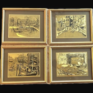 Peut inclure: Quatre estampes dorées encadrées représentant des scènes de port. Chaque estampe est dans un cadre doré avec un passe-partout marron. L'œuvre présente des bateaux, des bâtiments et des quais. Le style est vintage, avec des traits détaillés et une palette monochrome.
