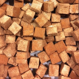 May include: A close-up image of a large pile of small, square, brown marshmallows covered in cinnamon. The marshmallows are arranged in a random pattern.