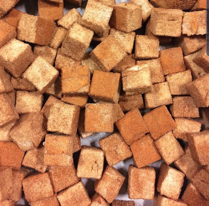 May include: A close-up image of a large pile of small, square, brown marshmallows covered in cinnamon. The marshmallows are arranged in a random pattern.