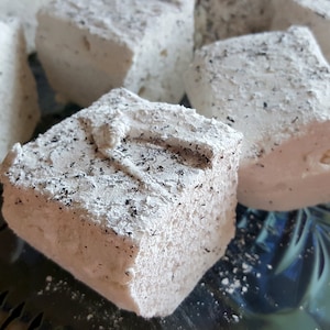 May include: Close-up of several white marshmallows dusted with powdered sugar. The marshmallows are arranged on a blue and green patterned surface.