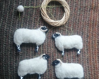 May include: A mobile with four white sheep with black faces and legs hanging from a woven wreath. The sheep are suspended from the wreath with green string.