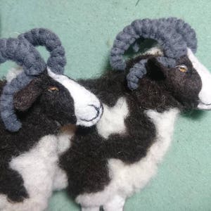 Puede incluir: Dos ovejas de fieltro blanco y negro con cuernos grises. Las ovejas est&aacute;n tumbadas con la cabeza girada hacia un lado.