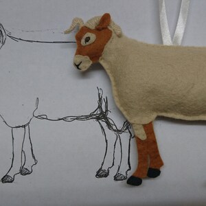 May include: A beige felt sheep ornament with brown legs and a black nose. The sheep is hanging from a white ribbon. A line drawing of a sheep is behind the ornament.