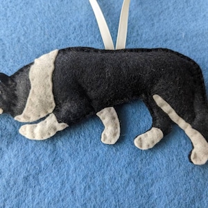 May include: A black and white felt ornament of a border collie dog. The ornament is hanging from a white ribbon.