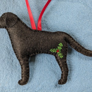 May include: Black felt ornament of a Labrador Retriever dog with green holly and red berries embroidered on its side.