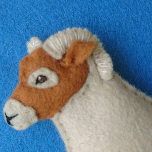 May include: A brown and white felt sheep toy with a white curly fleece and brown face. The sheep has a brown nose and a small black eye.