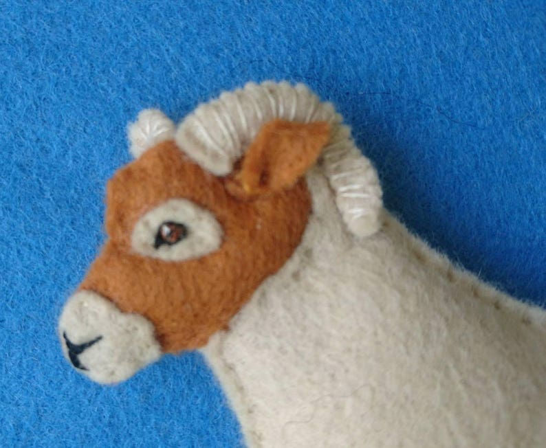 May include: A brown and white felt sheep toy with a white curly fleece and brown face. The sheep has a brown nose and a small black eye.