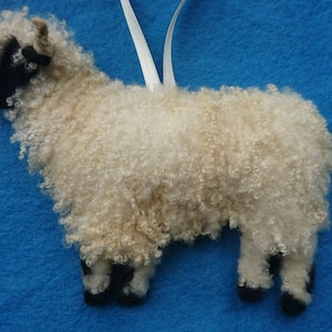 May include: A white and black sheep ornament with curly fleece. The sheep is standing on a blue background.