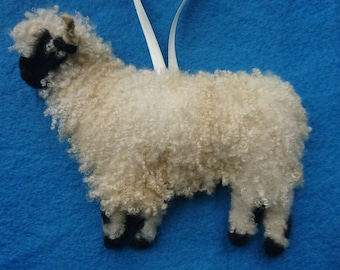 May include: A white and black sheep ornament with curly fleece. The sheep is standing on a blue background.