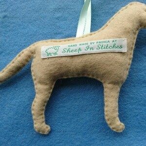 May include: A tan felt dog ornament with a white tag that reads "HAND MADE BY PAULA AT SHEEP IN STITCHES".