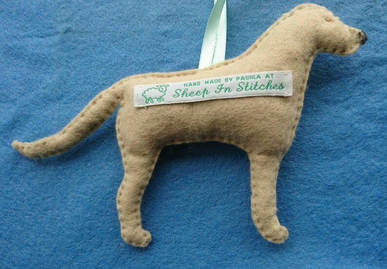 May include: A tan felt dog ornament with a white tag that reads "HAND MADE BY PAULA AT SHEEP IN STITCHES".