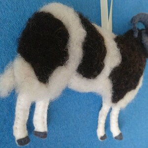 Puede incluir: Un adorno de oveja de fieltro blanco y negro con un cuerno rizado. La oveja est&aacute; de pie sobre sus cuatro patas y tiene una cara blanca.