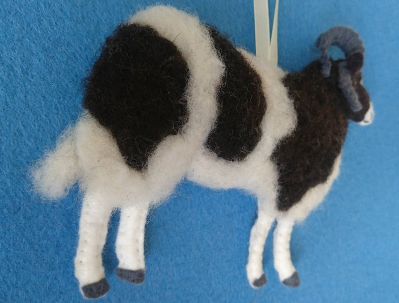 Puede incluir: Un adorno de oveja de fieltro blanco y negro con un cuerno rizado. La oveja est&aacute; de pie sobre sus cuatro patas y tiene una cara blanca.