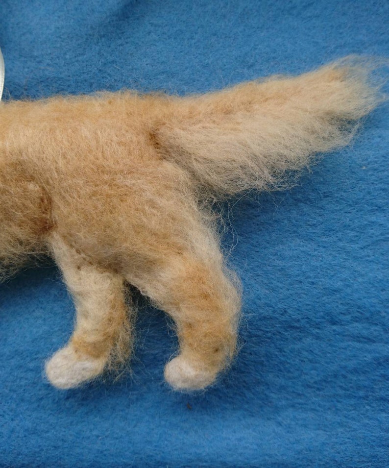 K&ouml;nnte beinhalten: Nahaufnahme eines hellbraunen Filztieres mit einem flauschigen Schwanz. Das Tier steht auf einer blauen Oberfl&auml;che.