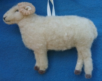 May include: A white felt sheep ornament with brown felt horns and hooves. The sheep is standing on a blue background.