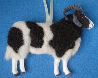 May include: A black and white felt sheep ornament with a gray curly horn. The sheep is standing on a blue background.