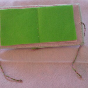 May include: A small green felt book with pink stitching and a pink and green string attached.
