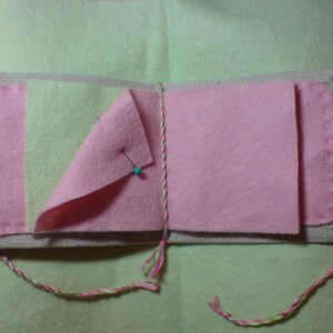 May include: A pink and green fabric book with a linen cover and a pin holding the pages together.