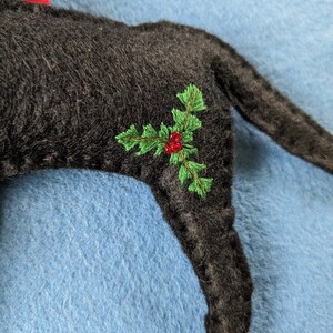 May include: Black felt Christmas ornament shaped like a dog with green holly and red berries embroidered on the side.