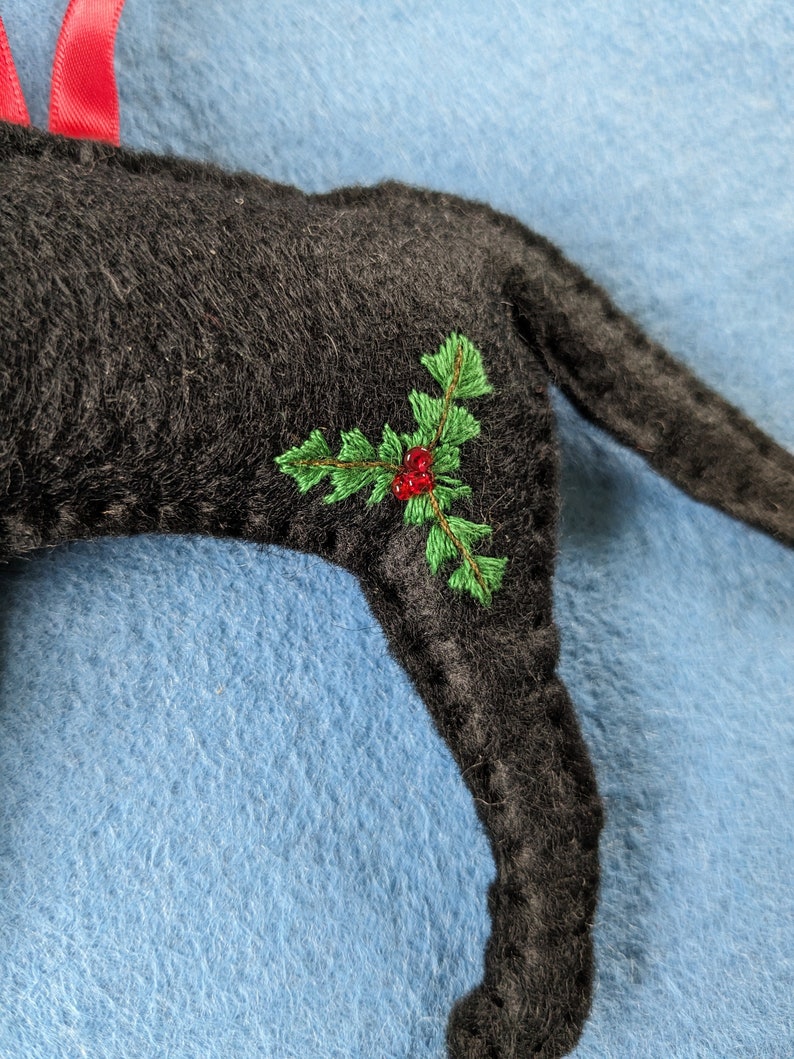 May include: Black felt Christmas ornament shaped like a dog with green holly and red berries embroidered on the side.