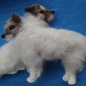 May include: Two white fluffy felted dogs, one with brown and black markings on its face, are posed together. The dog at the back is standing on its hind legs with its front paws resting on the dog in front of it.