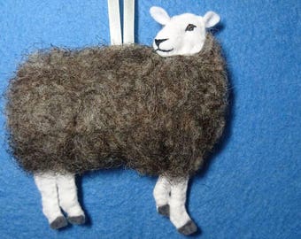 May include: A brown and white felt sheep ornament with a white face and black eyes. The sheep is hanging from a white string.