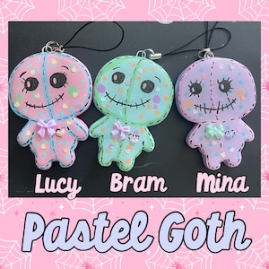 May include: Three pastel goth-style plush dolls with stitched faces and embroidered details. The dolls are pink, green, and purple with white polka dots and hearts. Each doll has a name tag: Lucy, Bram, and Mina.