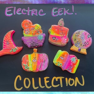 May include: Five colourful, hand-painted resin pins with a spooky Halloween theme. The pins feature a cauldron, a candle, a pumpkin, a book and a crystal ball. The text "Electric EEK! COLLECTION" is written on a black background.