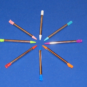 May include: Eight colorful stylus pens arranged in a starburst pattern on a blue background. The pens are silver with different colored tips, including pink, green, blue, orange, and purple.