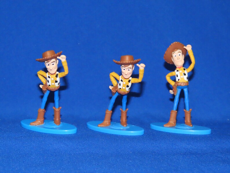 May include: Three plastic figurines of Woody from the Toy Story franchise. Each figurine is posed differently and stands on a blue base.