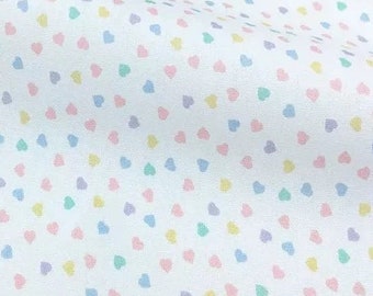 May include: White fabric with a repeating pattern of small pastel pink, blue, yellow, and green hearts.