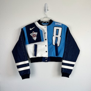Könnte beinhalten: Eine blaue, weiße und Jeans-Varsity-Jacke mit dem Wort "TITANS" und der Nummer "8" auf der Rückseite. Die Jacke hat einen weißen Nike-Swoosh auf der linken Brust und ein Teamlogo auf der rechten Brust.
