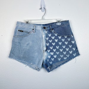 Puede incluir: Shorts vaqueros azul claro con un diseño único. Un lado presenta un lavado claro liso, mientras que el otro muestra un patrón de cabezas de Mickey Mouse blancas. Los shorts tienen un diseño clásico de cinco bolsillos y un dobladillo sin rematar.