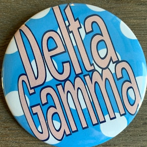 May include: A blue and white polka dot button with the text "Delta Gamma" in pink.